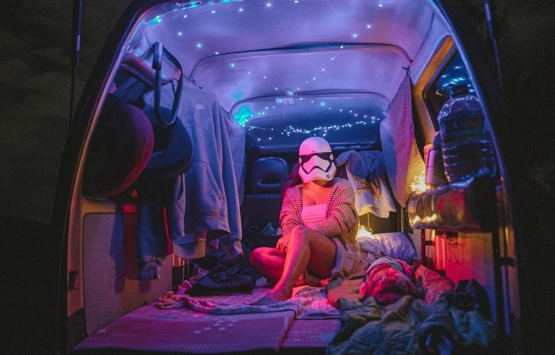 A woman wearing a storm trooper helmet sits inside a camper van.